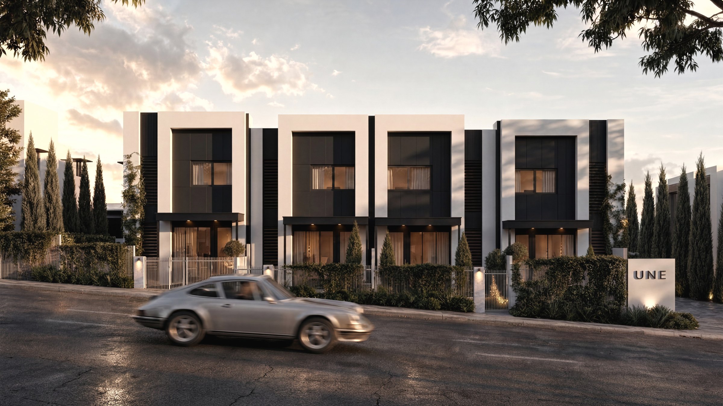 UNE — the full townhome row at dusk with the branded entry monolith