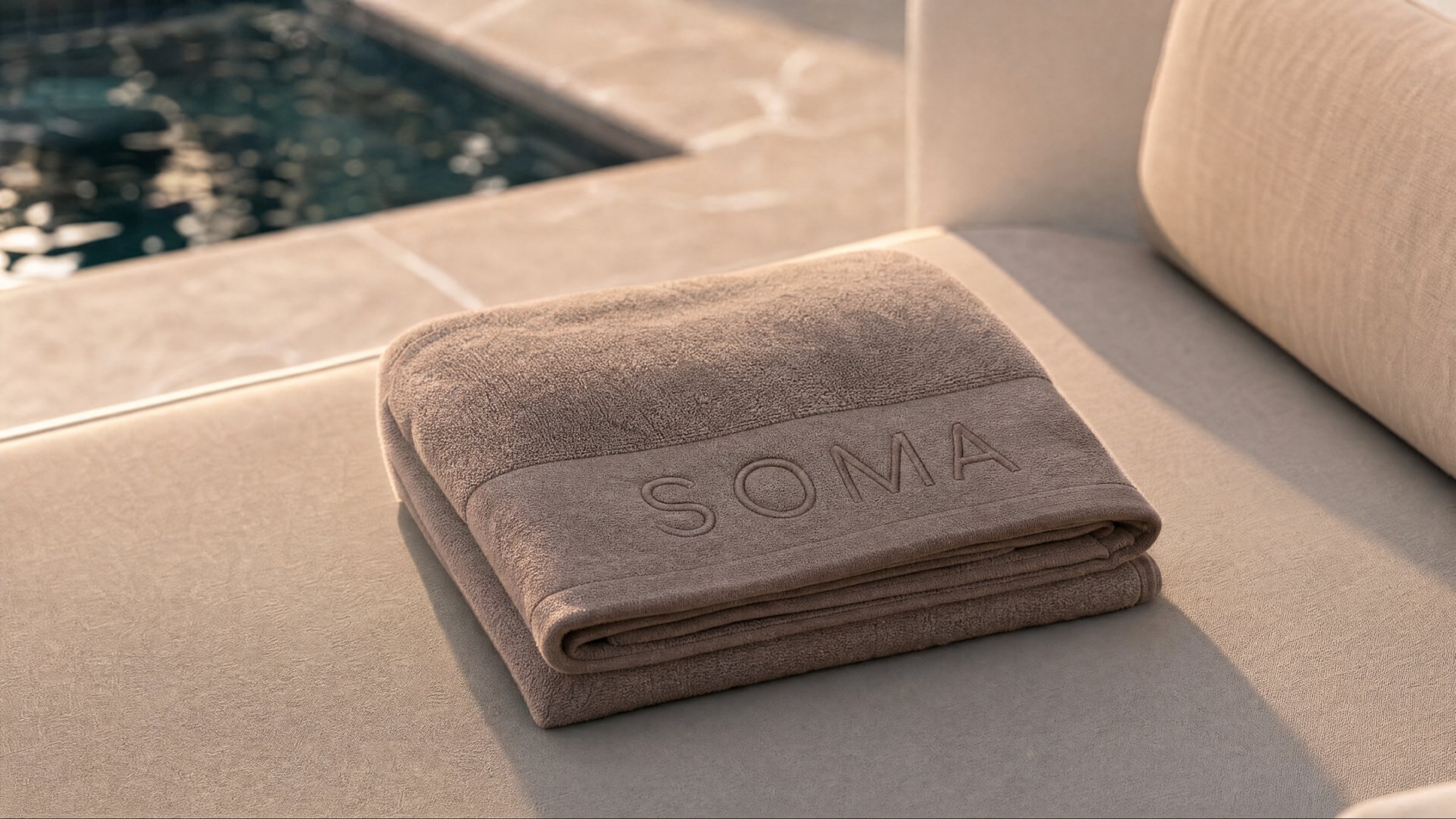 Soma — embroidered resident towel beside the pool
